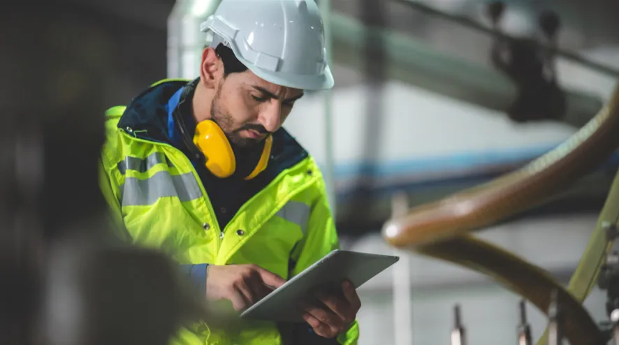 Construction worker in safety gear using a tablet at industrial worksites for roadway safety checks.